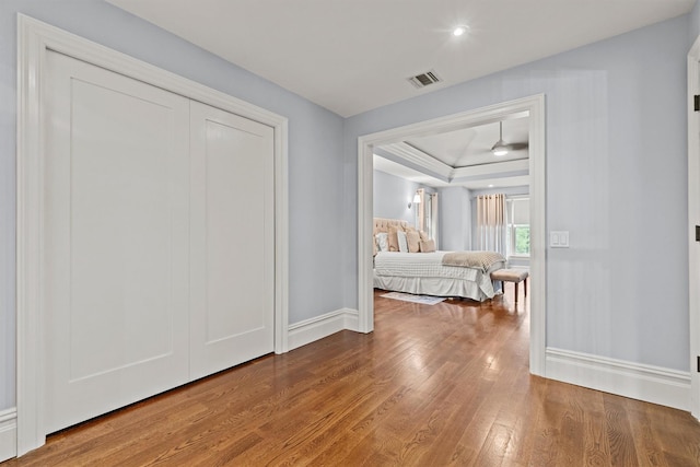 bedroom featuring a tray ceiling, wood finished floors, baseboards, and a closet