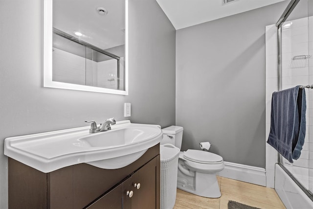 bathroom with toilet, wood finished floors, vanity, combined bath / shower with glass door, and baseboards