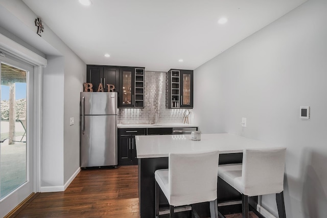 kitchen featuring freestanding refrigerator, a kitchen breakfast bar, tasteful backsplash, dark wood finished floors, and glass insert cabinets