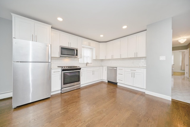 6629 74th St, Middle Village, NY 11379 - kitchen featuring appliances with stainless steel finishes, wood finished floors, decorative backsplash, white cabinetry, and recessed lighting