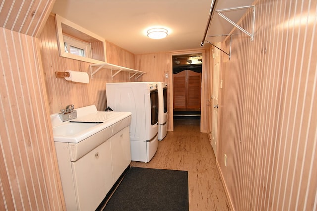 laundry room with washer and clothes dryer, wooden walls, and light wood-style flooring