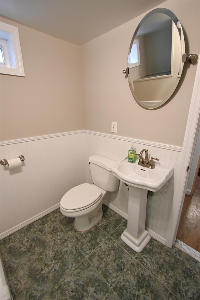 bathroom with a wainscoted wall, toilet, a sink, healthy amount of natural light, and baseboards