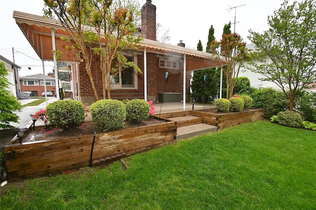 back of house featuring a chimney, brick siding, a yard, and a patio