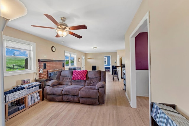 living area with light wood-style floors, a ceiling fan, a fireplace, and baseboards