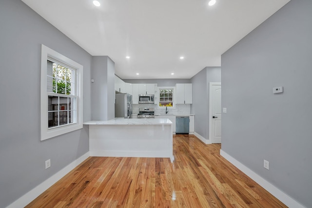 11827 219th St, Cambria Heights, NY 11411 - kitchen featuring appliances with stainless steel finishes, a peninsula, white cabinetry, baseboards, and light wood-style flooring