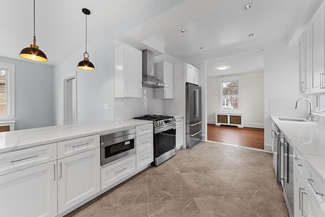 kitchen with stainless steel appliances, a sink, wall chimney range hood, light stone counters, and backsplash