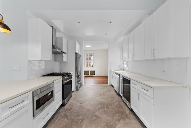 kitchen featuring stainless steel appliances, wall chimney exhaust hood, a sink, wine cooler, and white cabinets