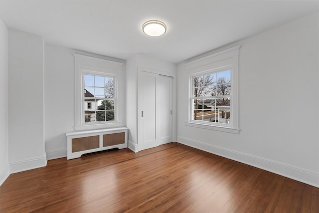 empty room featuring radiator, healthy amount of natural light, wood finished floors, and baseboards