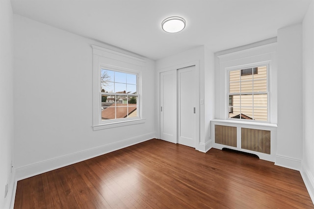 unfurnished bedroom with dark wood-style floors, baseboards, radiator heating unit, and a closet