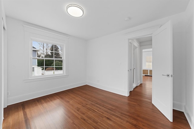 spare room featuring plenty of natural light, dark wood-type flooring, and baseboards