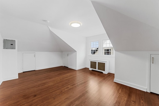 additional living space featuring wood finished floors, baseboards, lofted ceiling, electric panel, and radiator heating unit