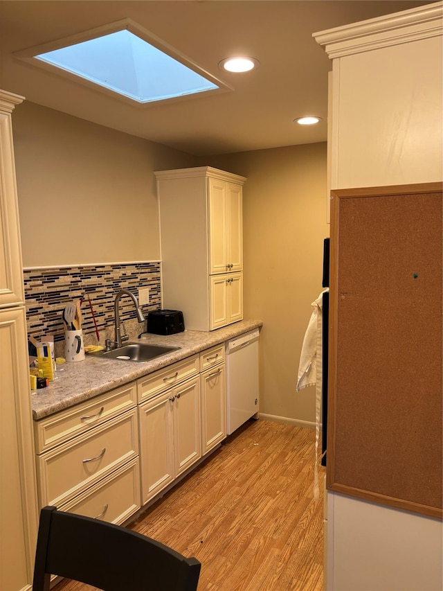 kitchen with dishwasher, a sink, light wood-style floors, a skylight, and decorative backsplash
