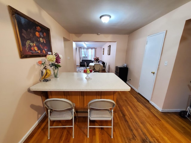 kitchen with a peninsula, wood finished floors, a breakfast bar, and baseboards