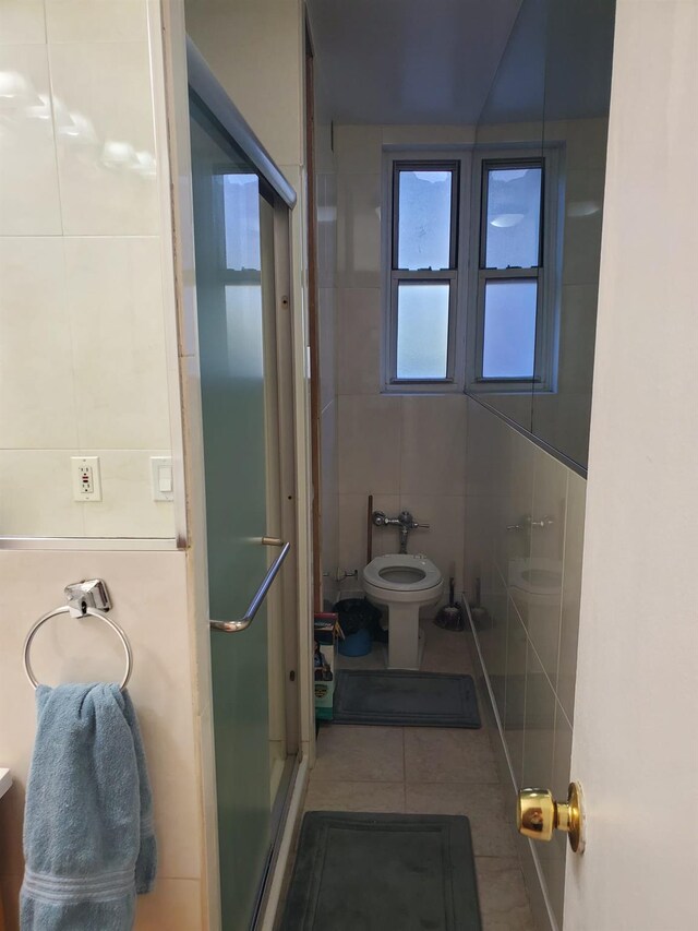 bathroom with tile walls, tile patterned floors, a shower stall, and toilet