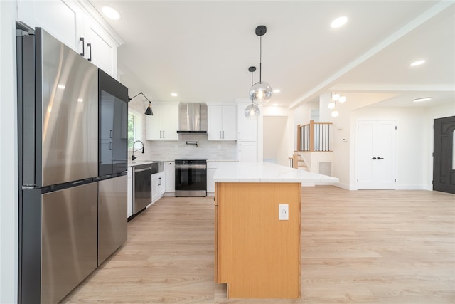 2001 Wellington Ct, Westbury, NY 11590 - kitchen featuring appliances with stainless steel finishes, wall chimney range hood, light wood-style flooring, a kitchen island, and light countertops