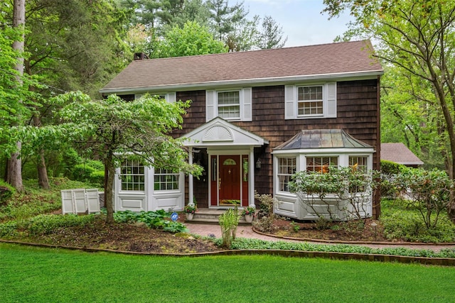 view of front facade featuring roof with shingles, a front lawn, and a chimney