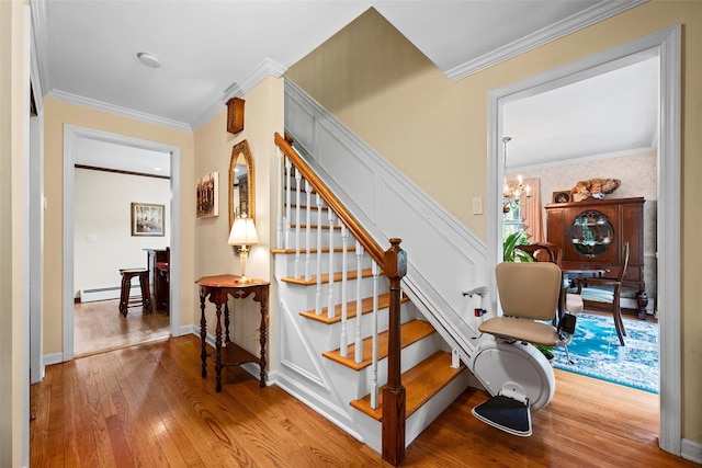staircase with wood-type flooring, a chandelier, ornamental molding, a baseboard heating unit, and baseboards