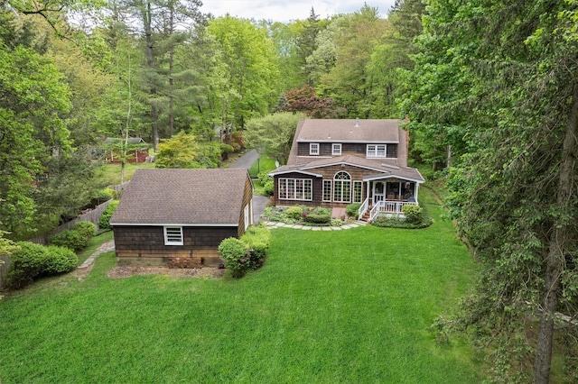 rear view of property featuring a lawn, an outbuilding, a forest view, and a storage shed