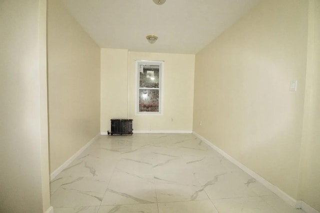 empty room featuring marble finish flooring, baseboards, and radiator