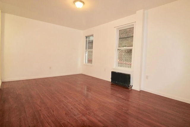 unfurnished room featuring radiator, dark wood-style floors, and baseboards
