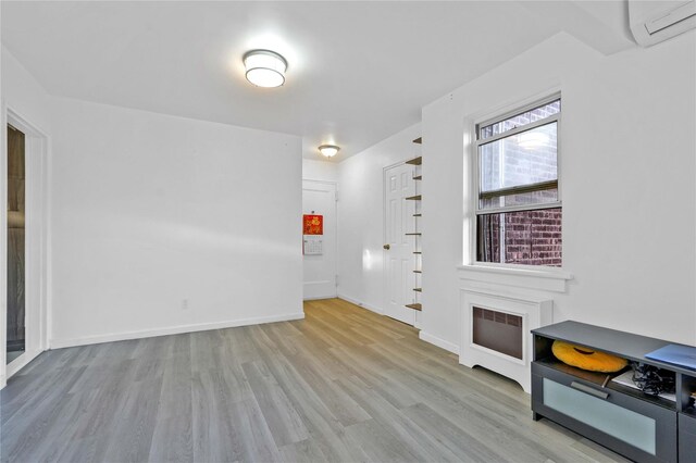 spare room with wood finished floors, a wall unit AC, and baseboards