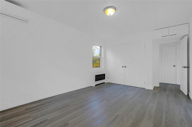 unfurnished room featuring an AC wall unit, wood finished floors, a fireplace, and heating unit