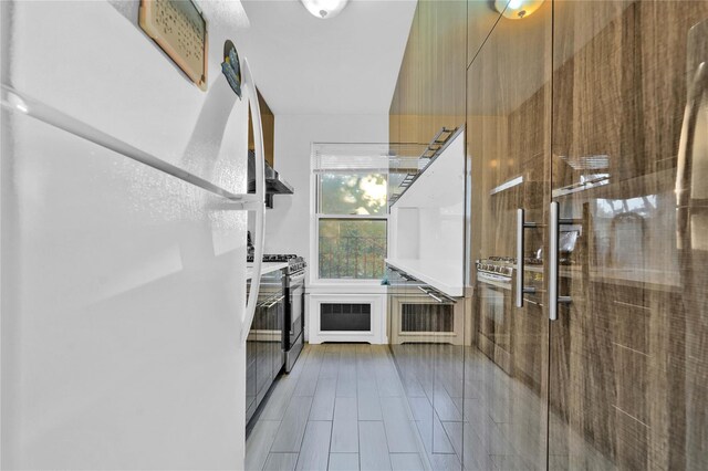 kitchen featuring freestanding refrigerator, modern cabinets, stainless steel gas range, brown cabinetry, and tile patterned flooring