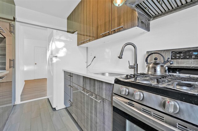 kitchen with gas stove, modern cabinets, a sink, light countertops, and wall chimney exhaust hood