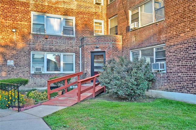 view of exterior entry with brick siding, a yard, and cooling unit