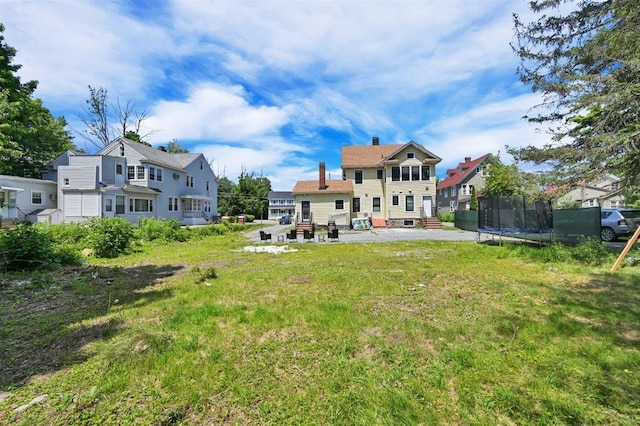 541 Broadway, Monticello, NY 12701 - back of property featuring a trampoline, a patio, a lawn, a chimney, and entry steps