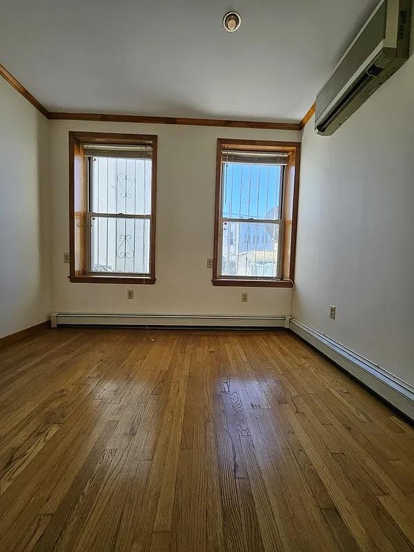 spare room featuring a wall mounted air conditioner, ornamental molding, wood finished floors, and baseboards