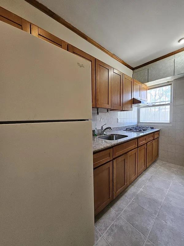 kitchen featuring freestanding refrigerator, a sink, stainless steel gas stovetop, ornamental molding, and light stone counters