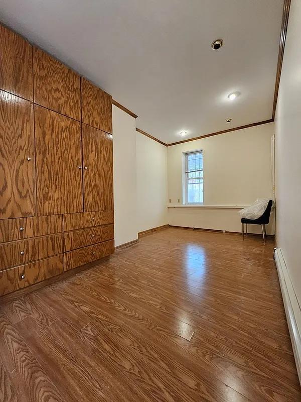 empty room featuring a baseboard radiator, crown molding, wood finished floors, and baseboards