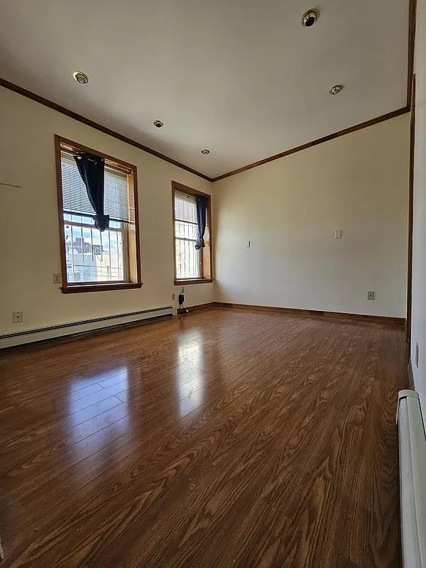 spare room featuring crown molding, a baseboard heating unit, wood finished floors, baseboards, and recessed lighting