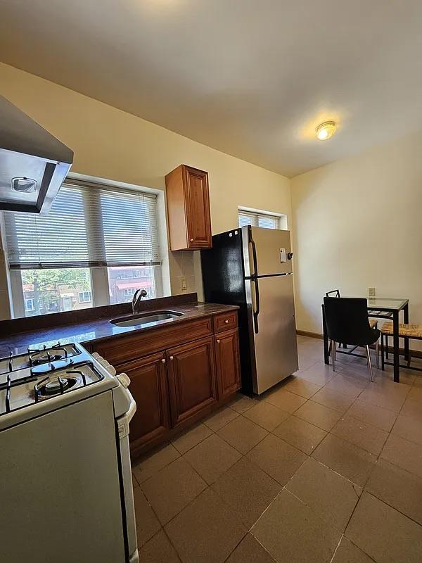 kitchen with a sink, freestanding refrigerator, dark countertops, white range with gas stovetop, and extractor fan
