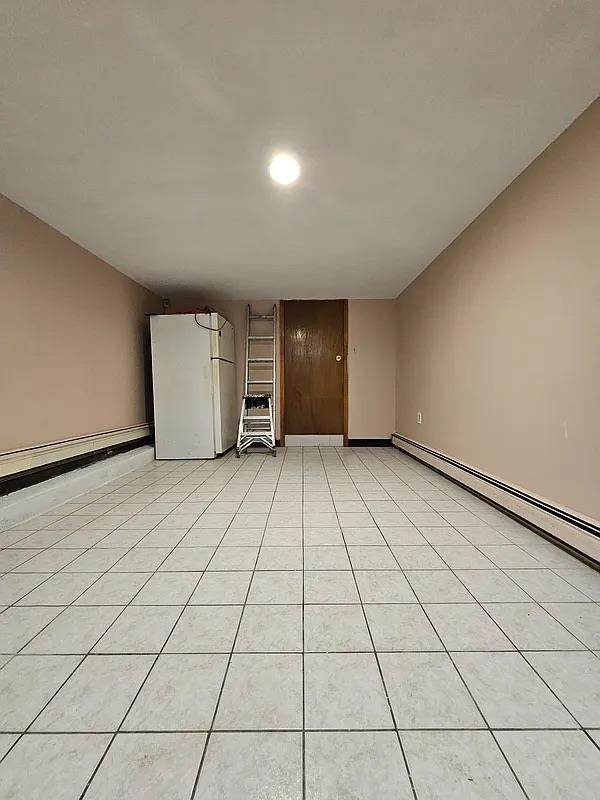 unfurnished living room with light tile patterned flooring and a baseboard heating unit