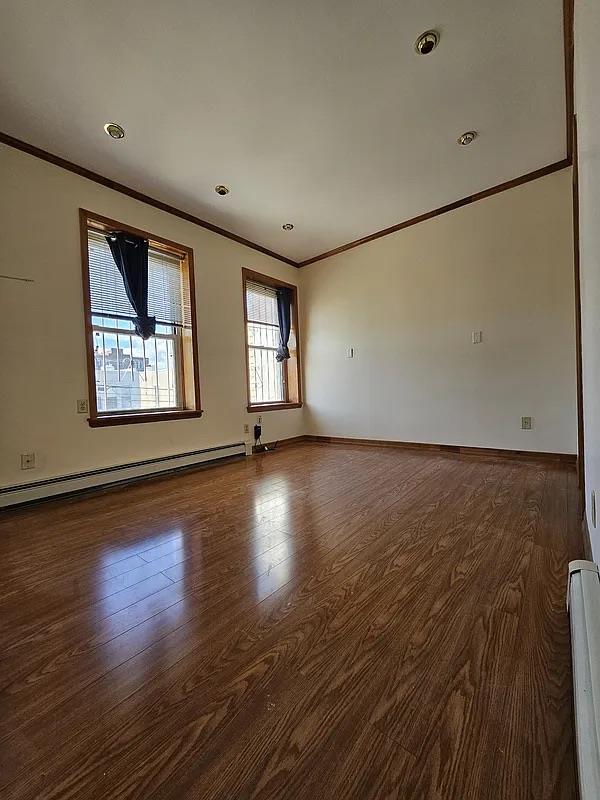 spare room featuring ornamental molding, baseboard heating, wood finished floors, baseboards, and a baseboard radiator