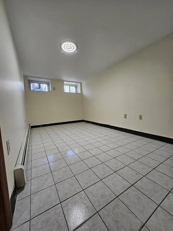 unfurnished room with a baseboard radiator, light tile patterned floors, and baseboards