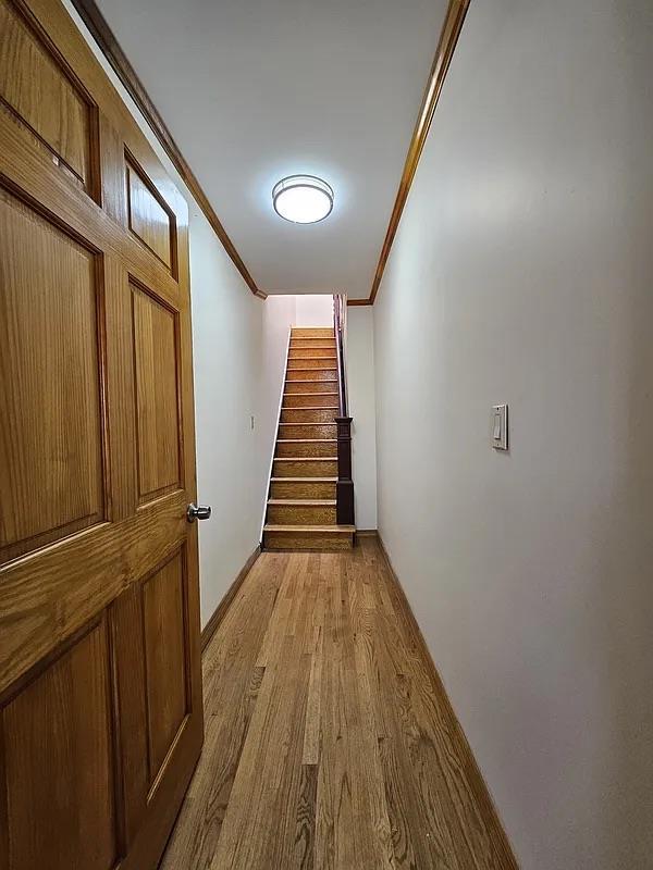hall with light wood-style floors, crown molding, and stairway