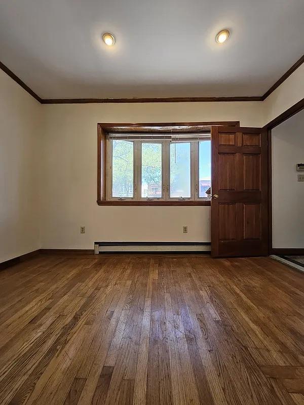 empty room with a baseboard radiator, crown molding, dark wood-style flooring, and baseboards