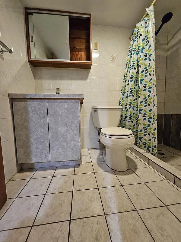 full bath with tile walls, a shower stall, vanity, toilet, and tile patterned flooring