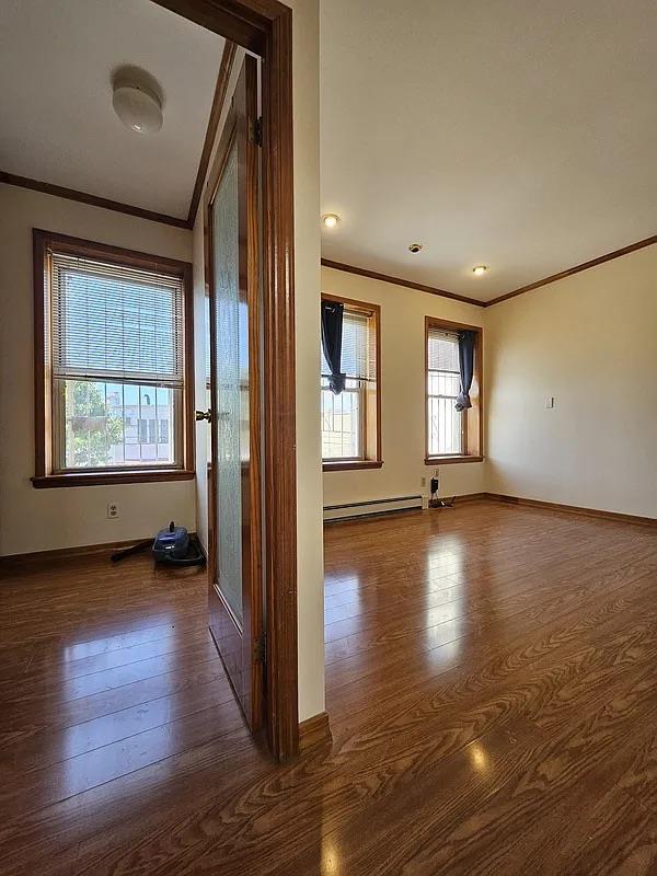 hall featuring crown molding, dark wood-style floors, baseboards, and a baseboard radiator