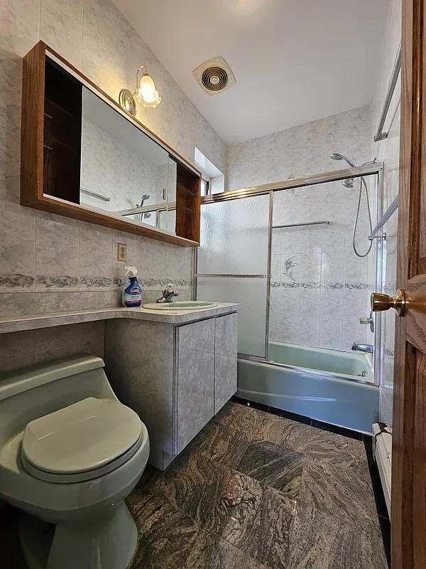 full bathroom with toilet, vanity, combined bath / shower with glass door, and tile walls