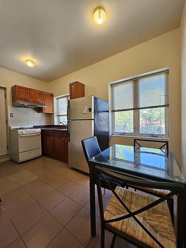 kitchen with white gas stove, freestanding refrigerator, tile patterned flooring, dark countertops, and brown cabinets
