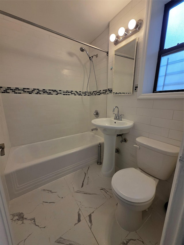 bathroom featuring toilet,  shower combination, marble finish flooring, tile walls, and a sink