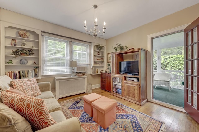 living room featuring radiator heating unit, a chandelier, light wood finished floors, built in shelves, and cooling unit
