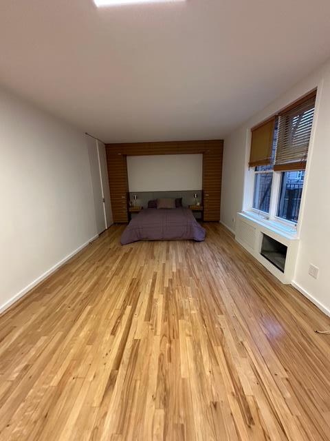 unfurnished bedroom featuring light wood-style flooring, a glass covered fireplace, and baseboards