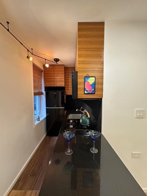 kitchen with freestanding refrigerator, dark wood-style flooring, brown cabinets, baseboards, and a sink