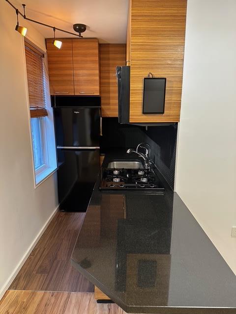 kitchen with freestanding refrigerator, a sink, baseboards, and dark countertops