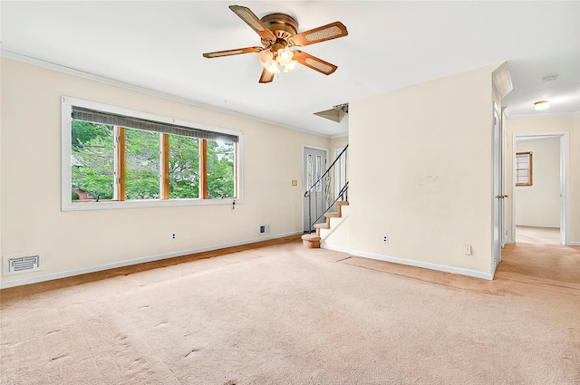 empty room featuring crown molding, light colored carpet, baseboards, ceiling fan, and stairway